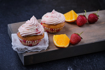 Orange cupcake with strawberry filling and butter cream with fresh berries. Dessert on a dark wooden board.