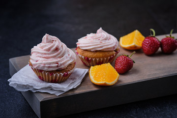 Orange cupcake with strawberry filling and butter cream with fresh berries. Dessert on a dark wooden board.