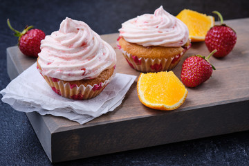 Orange cupcake with strawberry filling and butter cream with fresh berries. Dessert on a dark wooden board.