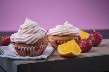 Orange cupcake with strawberry filling and butter cream with fresh berries. Dessert on a dark wooden board.