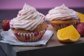 Orange cupcake with strawberry filling and butter cream with fresh berries. Dessert on a dark wooden board.