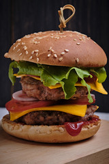A big classic american cheeseburger with two chops. Cheeseburger on a board, on a dark wooden background.
