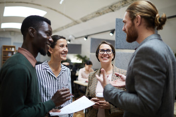 Waist up portrait of multi-ethnic group of business people laughing happily while chatting during...