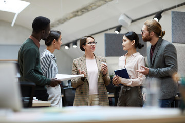 Portrait of successful businesswoman talking to employees while standing in modern office, copy...
