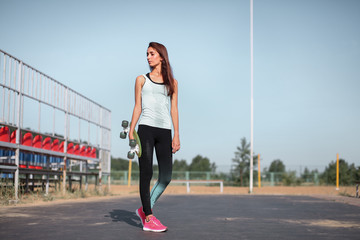 Teenager girl holding skateboard in hands on the cityscape background. Riding on scateboard. Summer concept of extreme sport. Close up portrait.