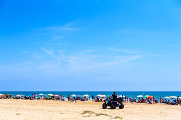 Fototapeta na wymiar Valencia, Spain - June 23, 2019: Police in quad patrolling a beach full of tourists and holiday makers to avoid thefts and thefts typical of the summer time.
