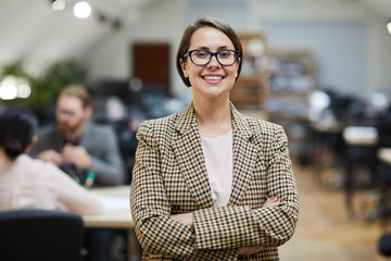Waist up portrait of successful businesswoman smiling at camera while posing in office standing...