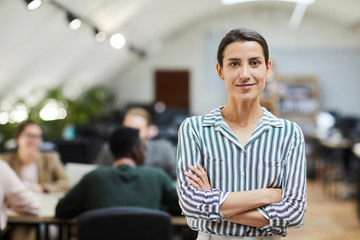 Waist up portrait of confident businesswoman looking at camera while posing in office standing with...