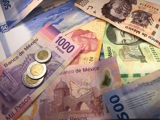 Many mixed Mexican peso bills spread over a wooden desk