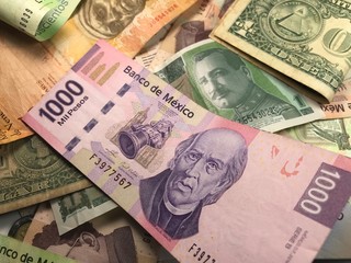 Many mixed Mexican peso bills spread over a wooden desk