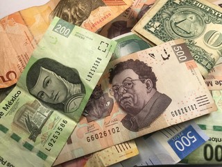 Many mixed Mexican peso bills spread over a wooden desk