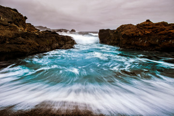 Turquoise and White Water in Motion as Surf Rolls onto Shore under Gray Sky