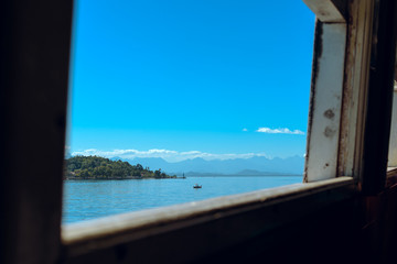 Fototapeta na wymiar Beautiful view through the window of a boat of the clear blue sky reflecting in the sea water with mountains in the background and a fisherman in the middle of the waters of Guanabara Bay in Rio.