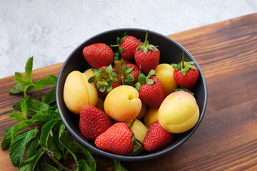 Strawberries and apricots decorated with mint leaves. Bowl with fresh sweet summer fruits.