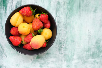 Strawberries and apricots on green wooden board. Copy space. Bowl with fresh summer fruits.
