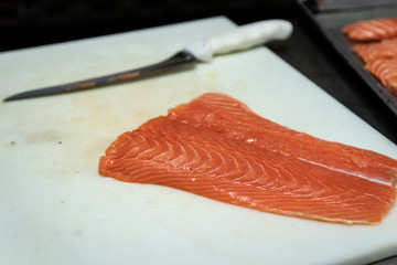 Raw filet of salmon on white cutting board with chef knife