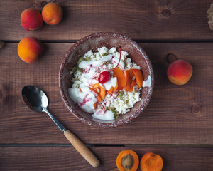 Breakfast of cottage cheese with fresh apricots and cherries in a deep ceramic plate on a wooden...