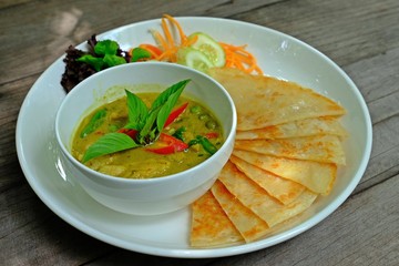Thai green chicken curry and roti in white plate on wooden table.
