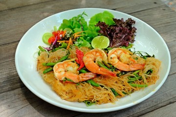 Fried Spicy Rice Vermicelli With Shrimp and Water Minosa in white plate on wooden table.