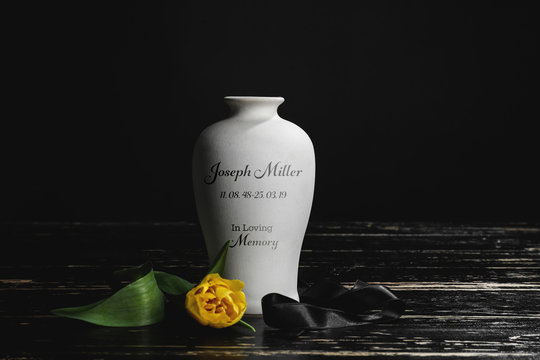 Mortuary urn with ribbon and flower on table against dark background