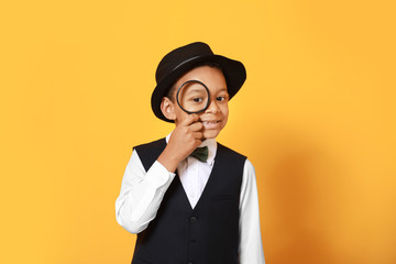 Little African-American detective with magnifier on color background