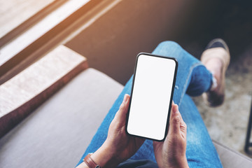 Top view mockup image of woman holding black mobile phone with blank screen while sitting in cafe