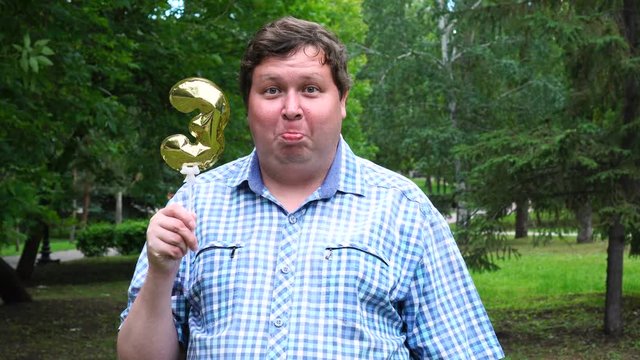 Big man holding golden balloon making the 3 number outdoor. 3th anniversary celebration party