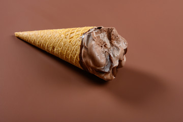 side view coffee and chocolate flavor ice cream cone with couple of bites on brown background