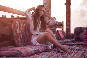 Young fashion eastern woman in white dress relaxing in traditional oriental interior in arabic town.