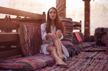 Obraz premium Young fashion eastern woman in white dress relaxing in traditional oriental interior in arabic town.