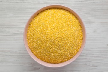 Organic Masarepa corn meal in a pink bowl over white wooden surface, top view. Overhead, from above. Close-up.