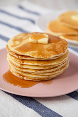 Stack of homemade pancakes with butter and maple syrup on a pink plate, side view. Closeup.