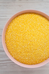 Dry organic Masarepa corn meal in a pink bowl over white wooden background, top view. Close-up.