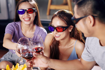 Happy young men and women in 3D glasses laughing and drinking wine when watching movie together