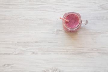 Glass jar with smoothie made of banana, black currant, coconut milk on a white wooden table, top view. Overhead, from above. Copy space.