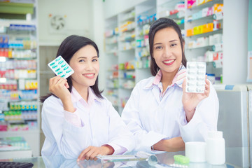 Two asian female pharmacist holding medicine and smile in pharmacy (chemist shop or drugstore)