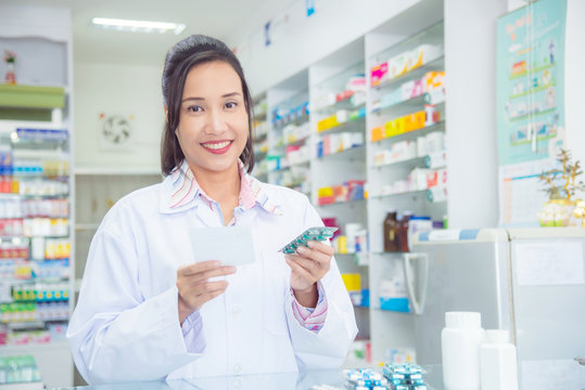 Smiling asian female pharmacist holding medicine and smile in pharmacy (chemist shop or drugstore)