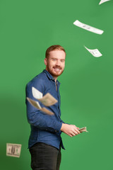 Happy successful rich young man throwing money in the air, isolated on green