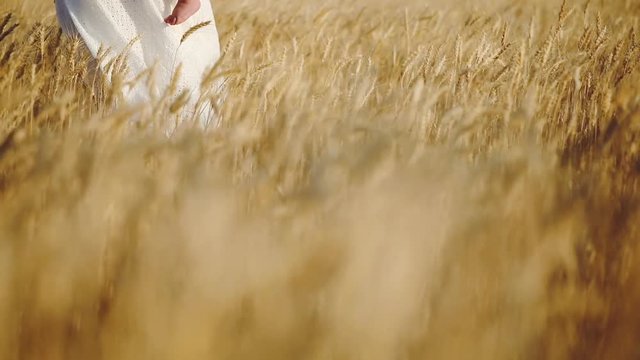 woman in long white lacy dress straw hat with toddler in arms walks along ripe wheat field low angle shot slow motion