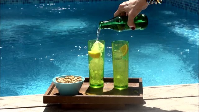 Woman filling the glasses with soda on the pool deck.