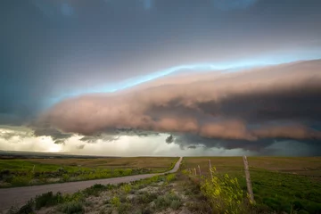 Fotobehang A dirt road in the countryside leads to the shelf cloud of a severe storm in the evening light. © Dan Ross