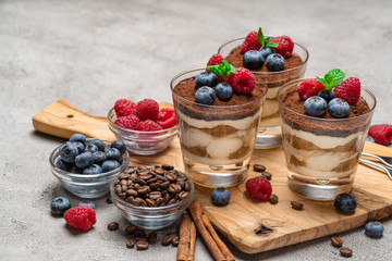 Classic tiramisu dessert with blueberries and raspberries in a glass on concrete background