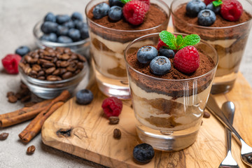 Classic tiramisu dessert with blueberries and raspberries in a glass on concrete background