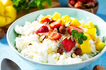 Dietary breakfast for summer time. Fresh cottage cheese close-up with strawberry, mango and nuts on a light blue stone or slate table.
