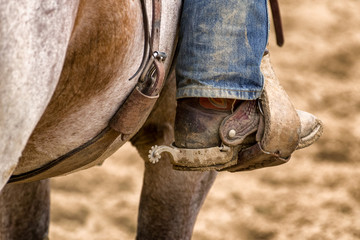 Close up detail of cowboy boot with spur in stirrup on horse during western rodeo