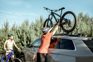 Young couple preparing for the bicycle riding, picking up mountain bicycle from the car trunk...