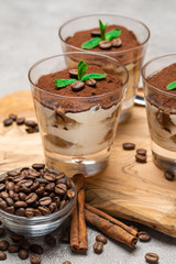 Classic tiramisu dessert in a glass cup on wooden cutting board on concrete background