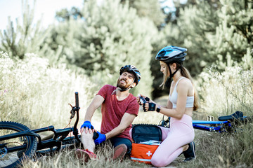 Naklejka premium Woman giving first aid to a man with knee injury while cycling on the mountain bicycles on the forest road during the summer time