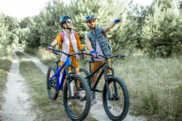 Young couple traveling with mountain bicycles in the forest, man showing with hand on the way...