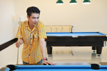 young adult asian man looking final billiard or snooker ball with concentration and happy face during the game in snooker club.